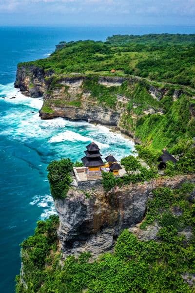 Clifftop temple overlooking turquoise ocean waves and lush green cliffs in Bali, Indonesia